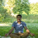 Man practicing meditation in a peaceful park, surrounded by nature, promoting wellness and inner peace.